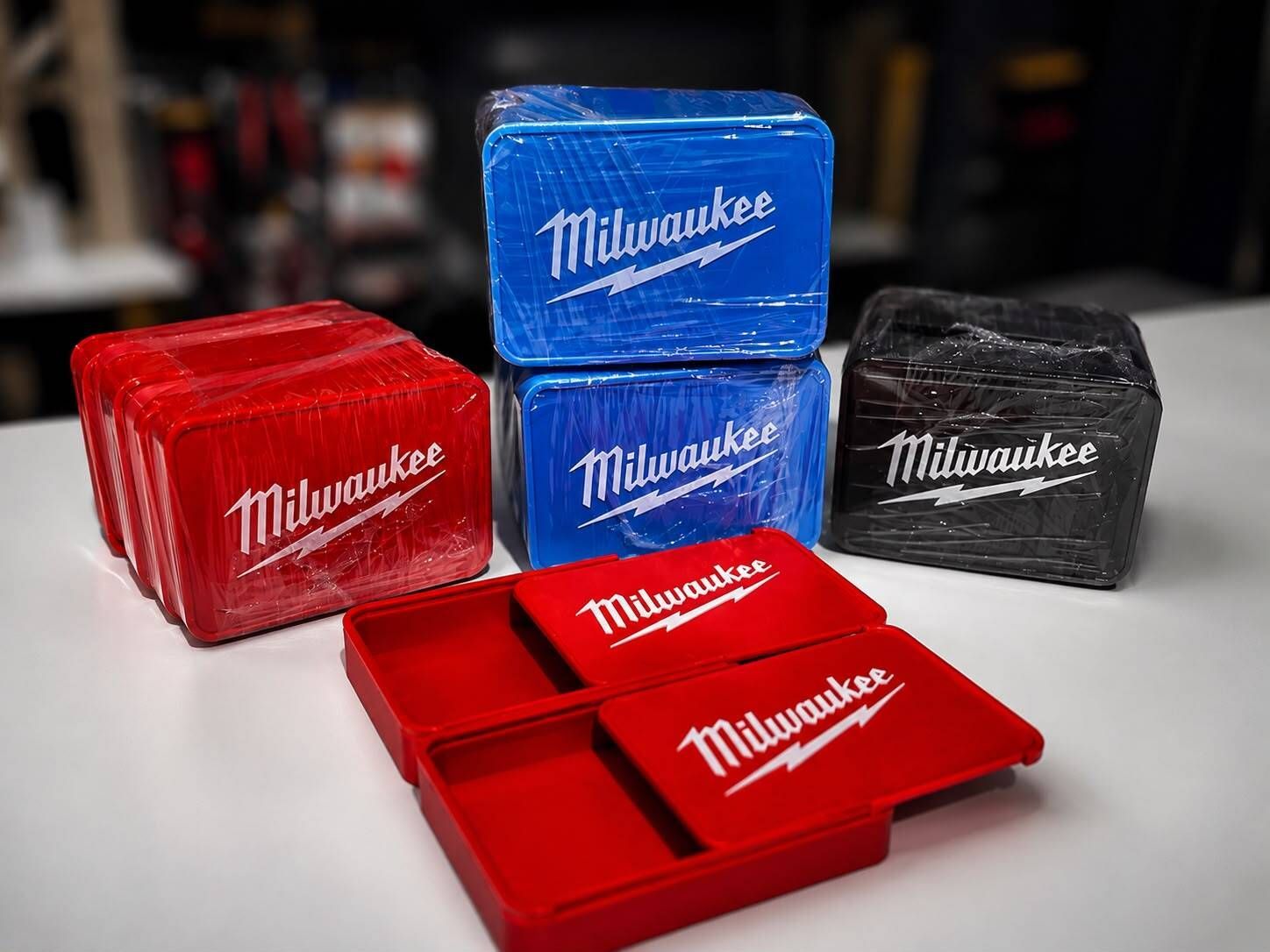 Estuches organizadores de herramientas Milwaukee en rojo, azul y negro sobre una superficie oscura.