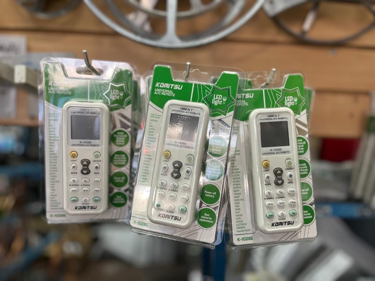 Tres mandos a distancia blancos, empaquetados y colgados en el pasillo de una tienda, con etiquetas verdes y blancas.