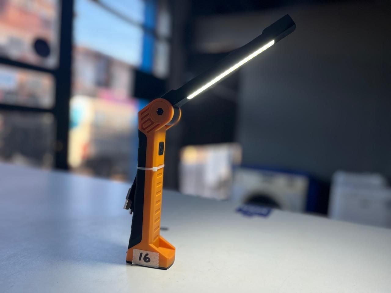 Minilámpara de escritorio naranja brillando sobre una mesa blanca con un fondo interior desenfocado.