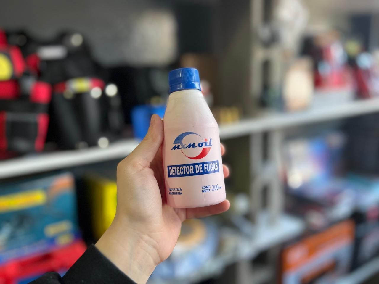 Una mano sostiene una pequeña botella rosa con tapa azul frente a unas estanterías de tienda borrosas.