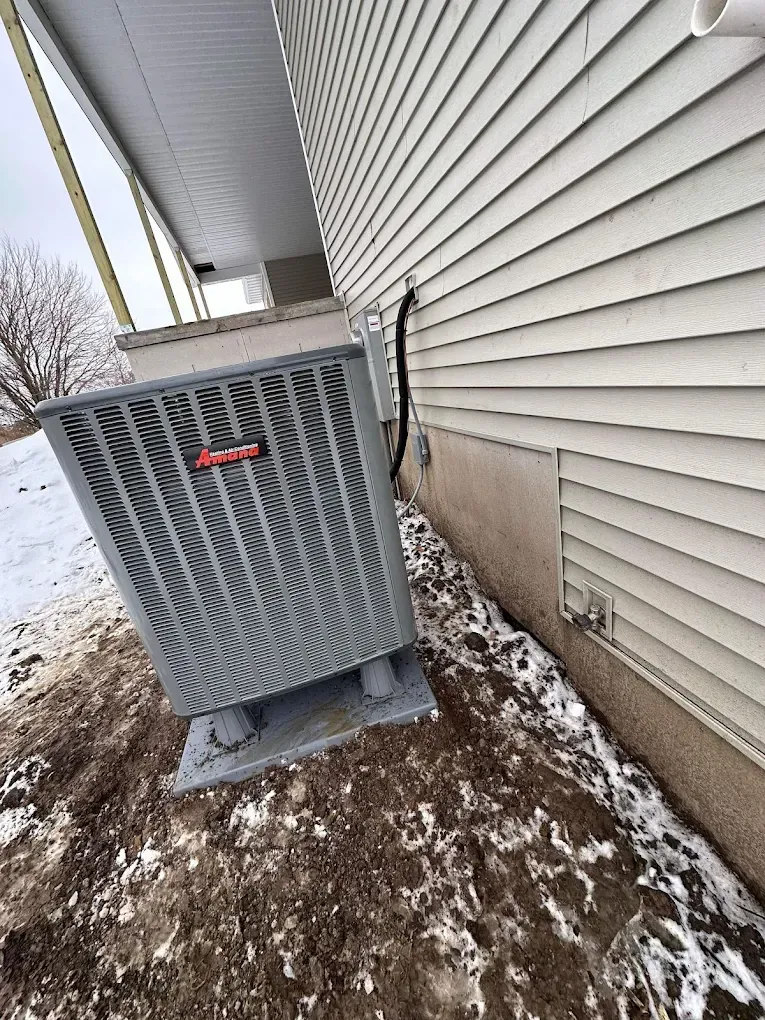 Air conditioning unit next to a house with black electrical conduit. Snowy ground.