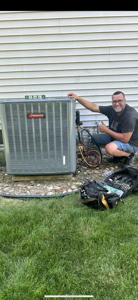 Man giving thumbs up next to an Armstrong air conditioning unit. Outdoors, grass and siding background.
