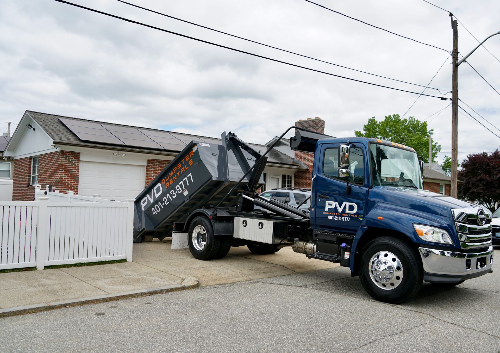 A large black dumpster is parked in front of a brick house.