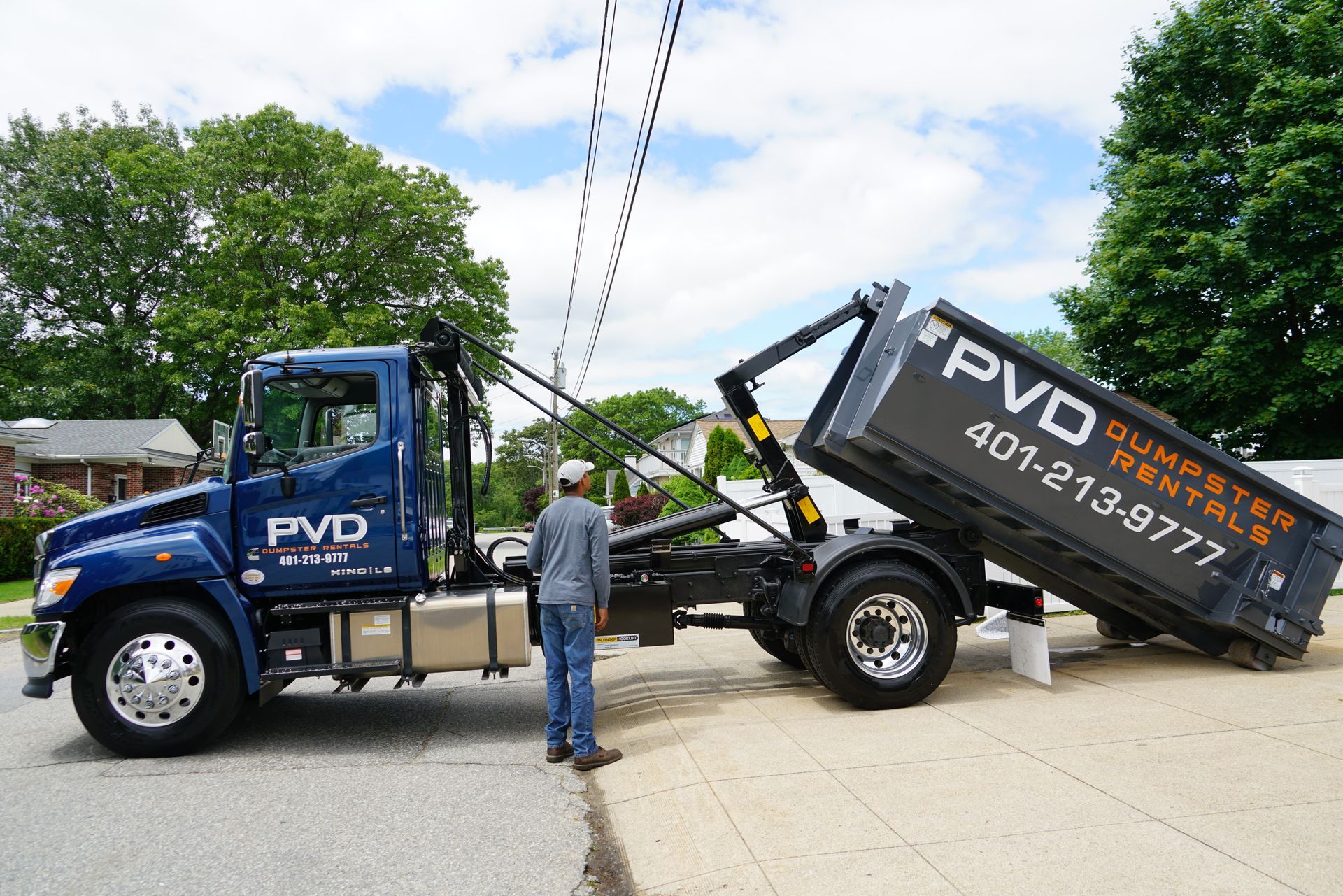 A large black dumpster is parked in front of a brick house.