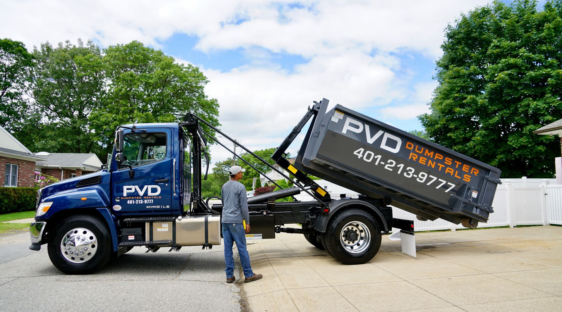 A large black dumpster is parked in front of a brick house.