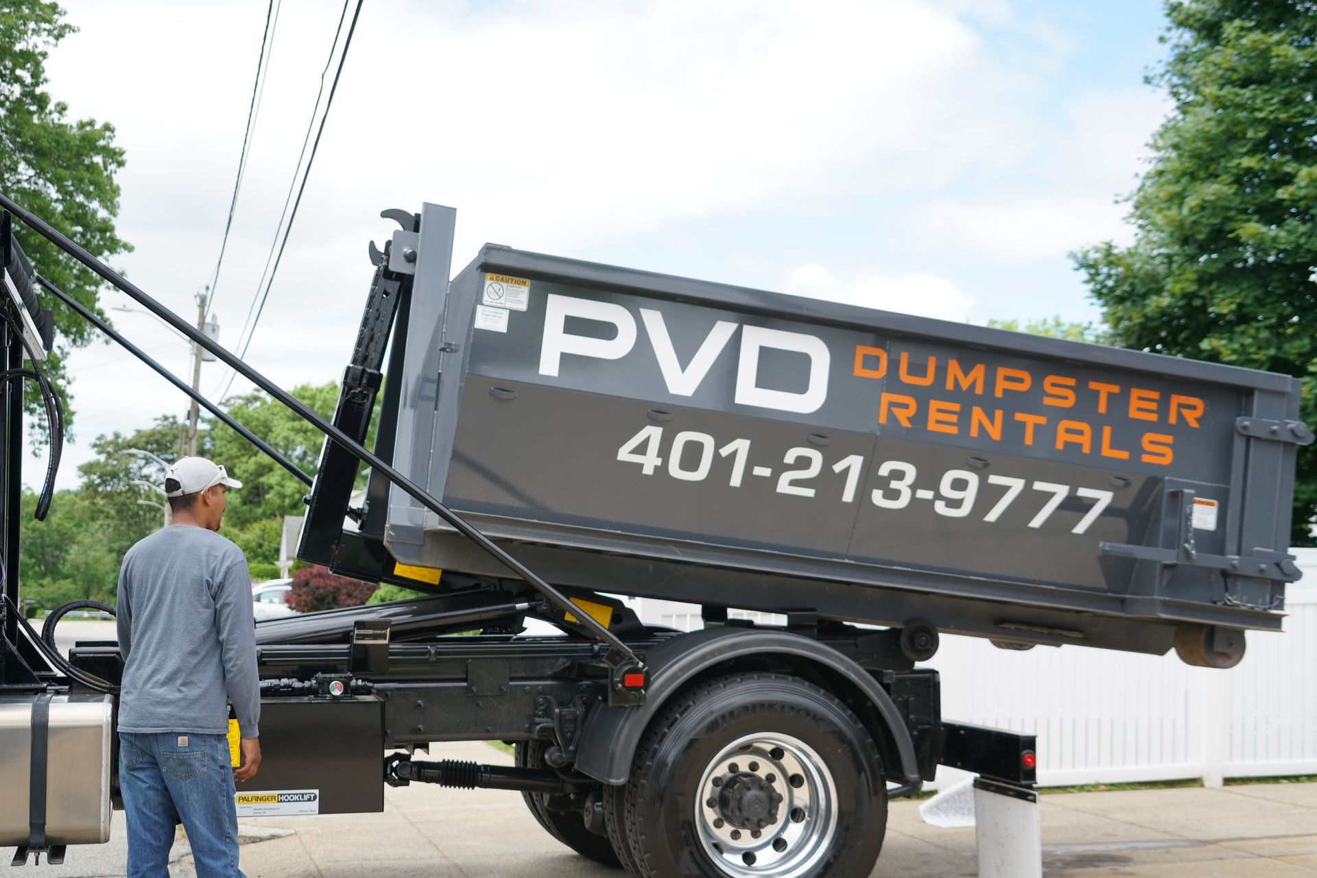 A white dump truck is pulling a black dumpster on a dirt road.