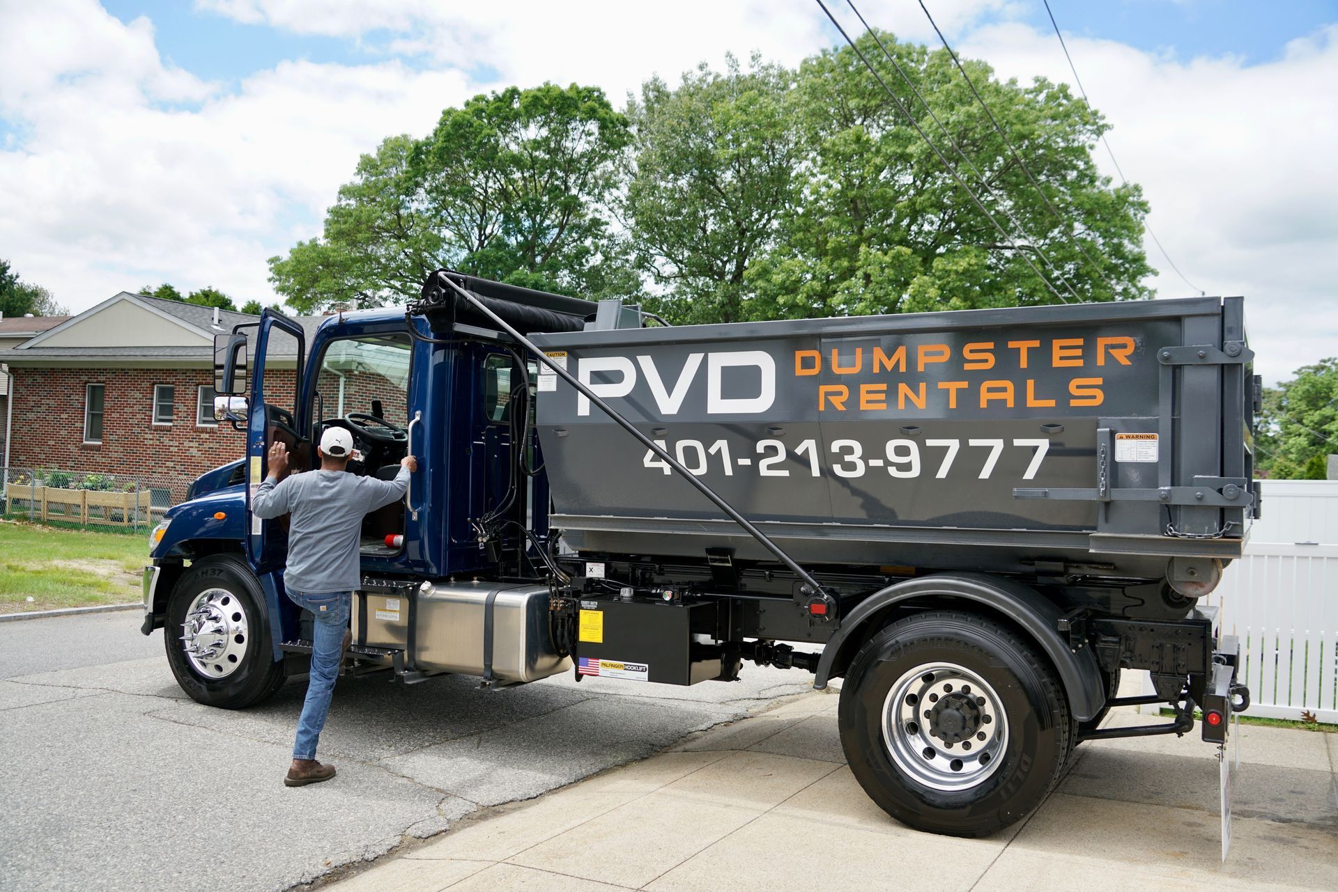 A large black dumpster is parked in front of a brick house.