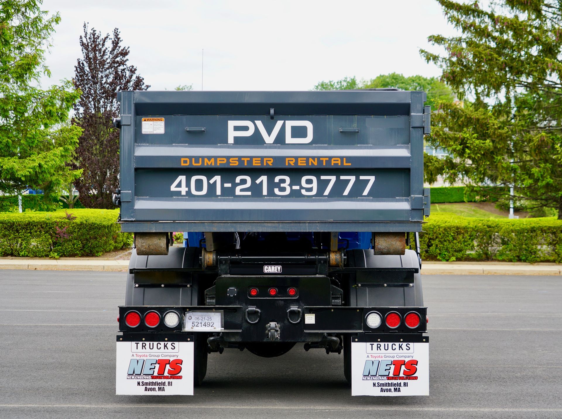 A large black dumpster is parked in front of a brick house.