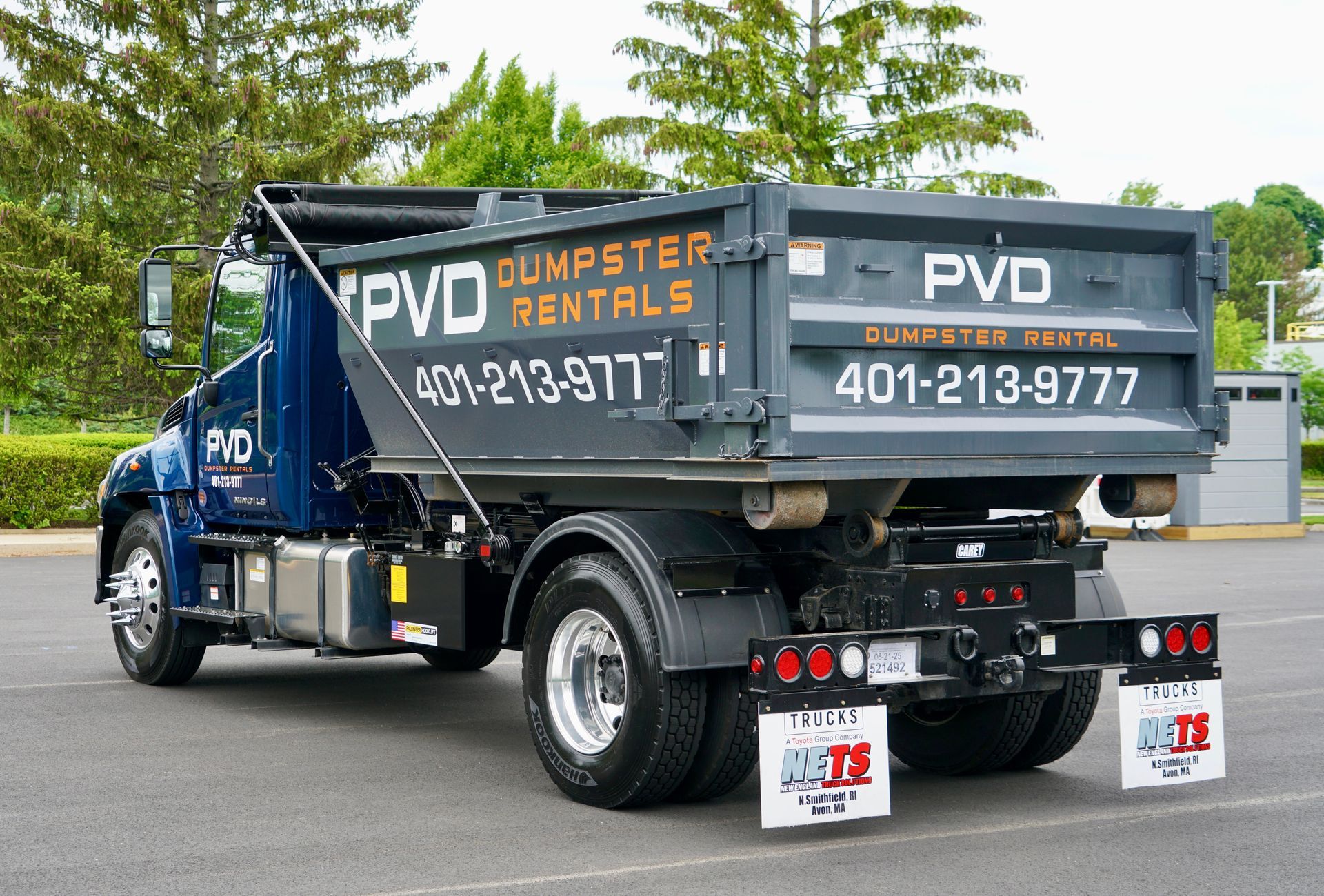 A large black dumpster is parked in front of a brick house.