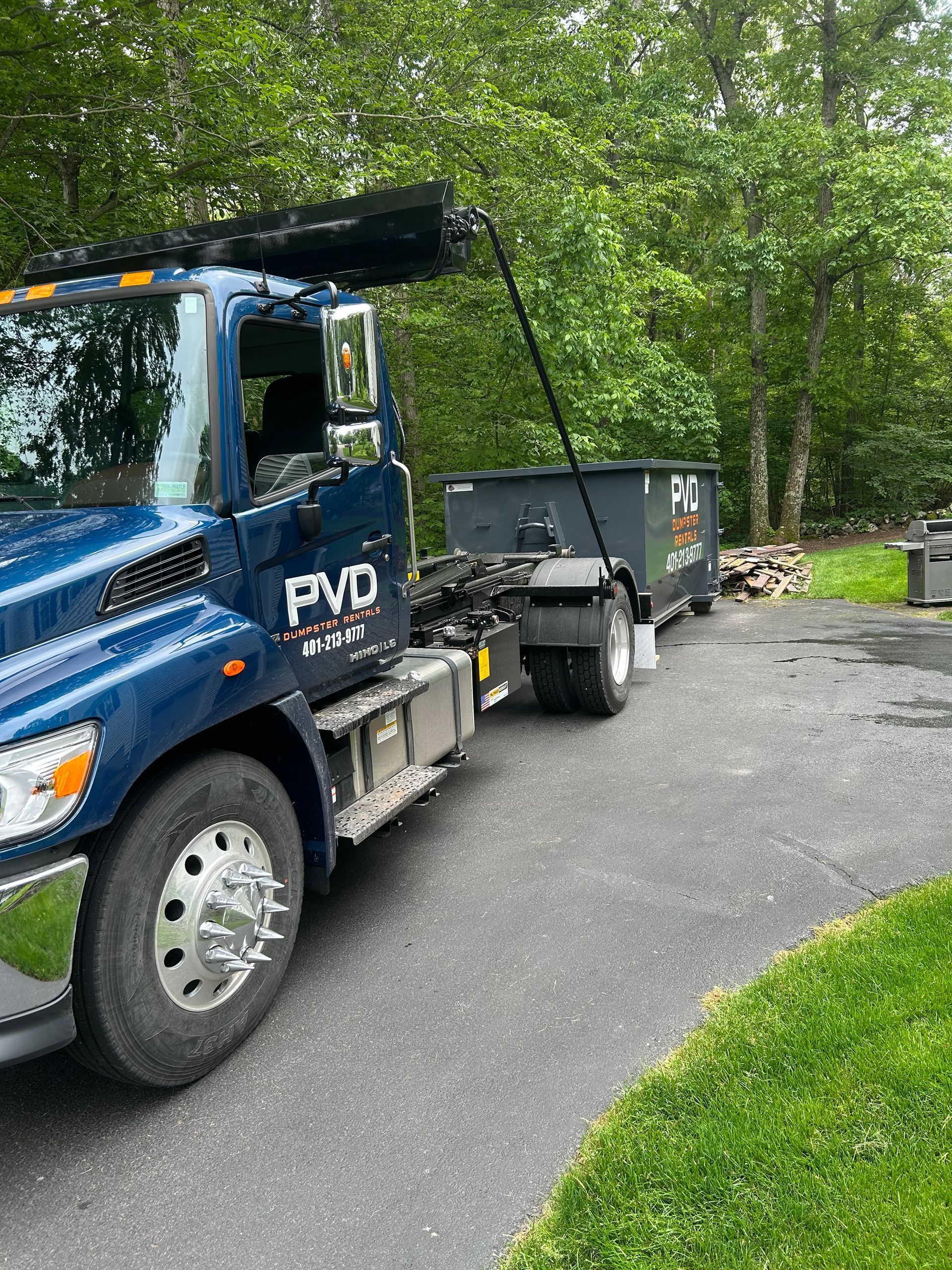 A large black dumpster is parked in front of a brick house.