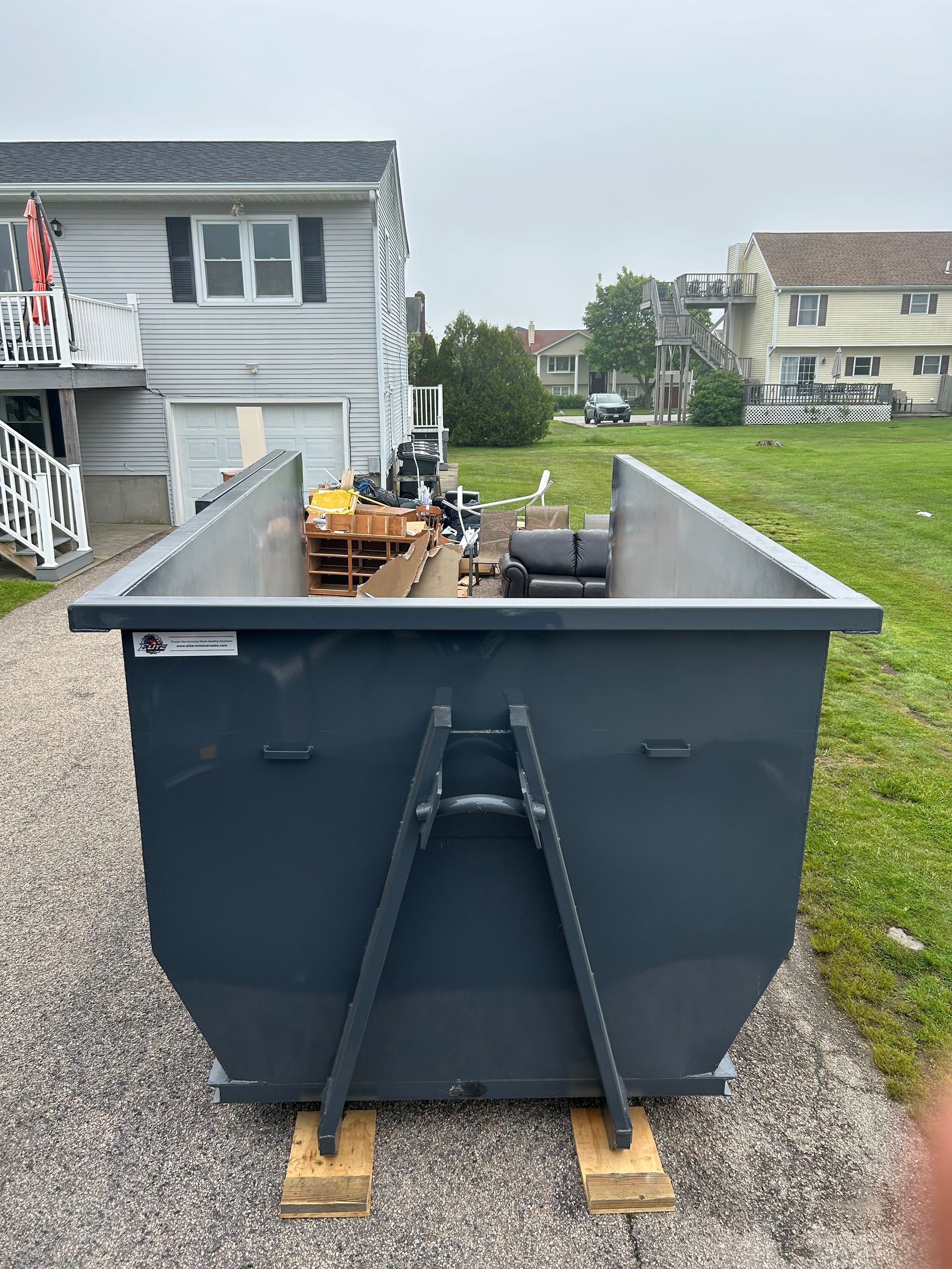 A dumpster filled with wood and rocks is sitting in front of a building under construction.
