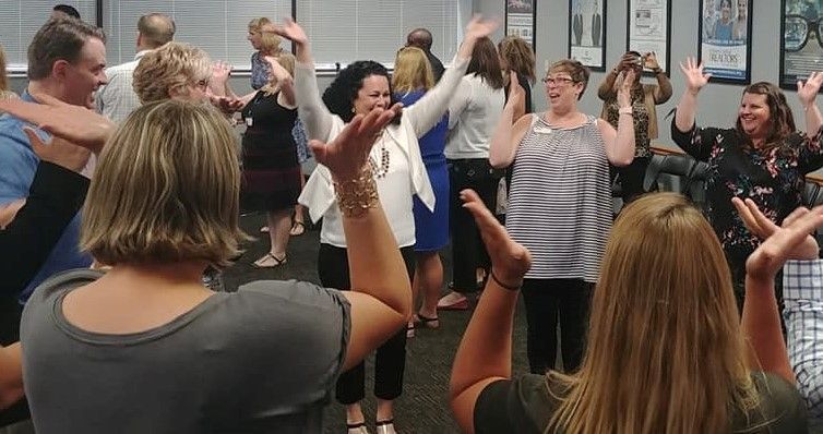 A group of people are dancing in a circle with their hands in the air.