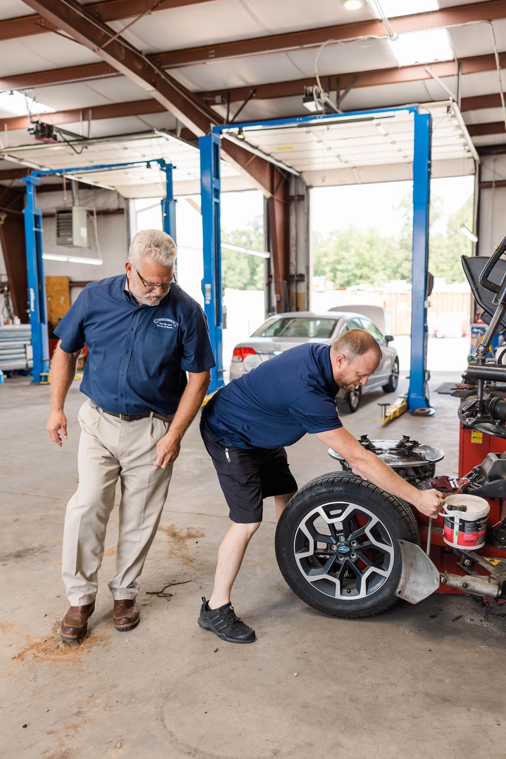 Two men in a garage, one looking at a tire as the other works on it with equipment | Stephen's Automotive