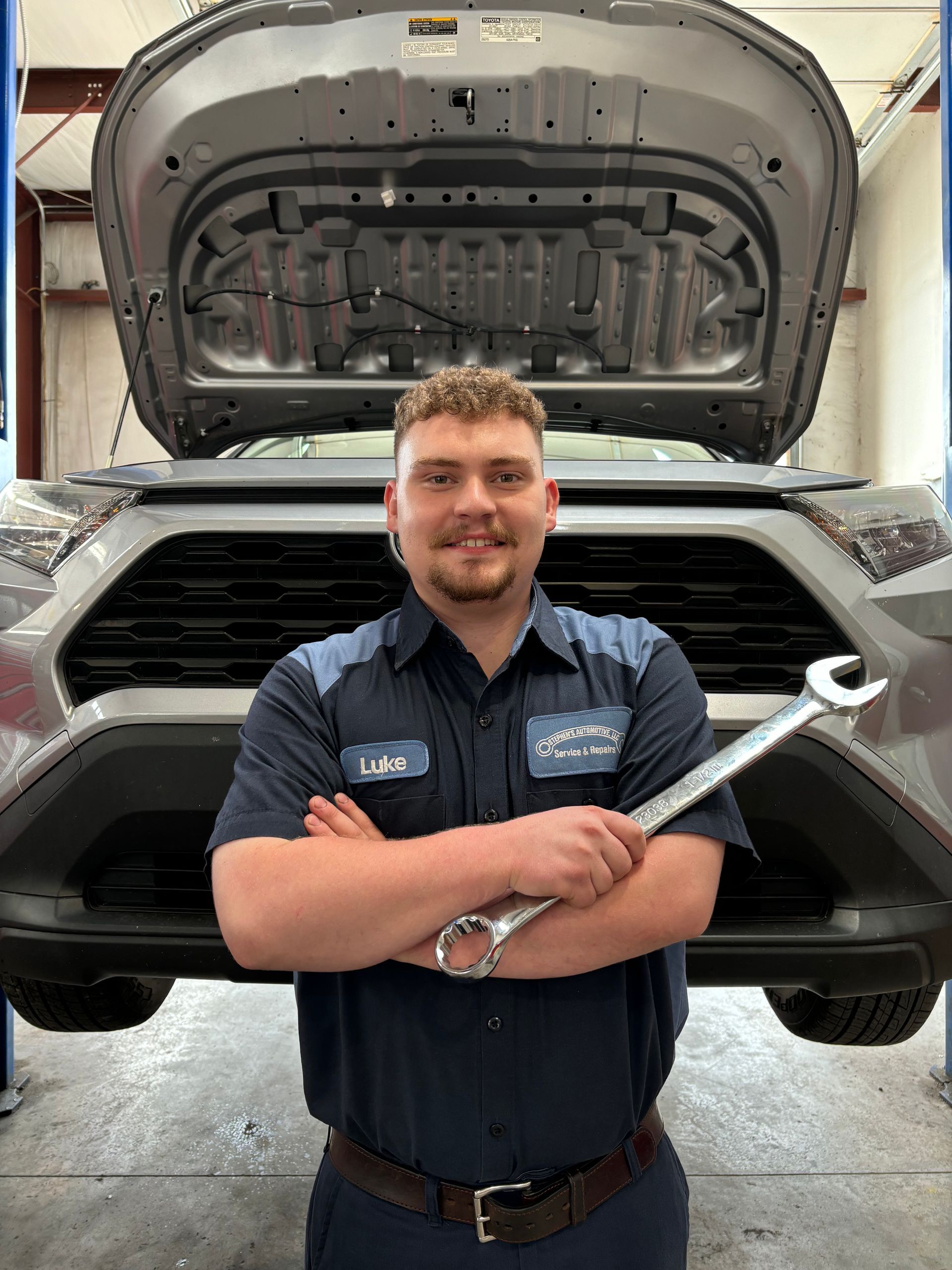 Mechanic holding a wrench; in front of a car with an open hood | Stephen's Automotive