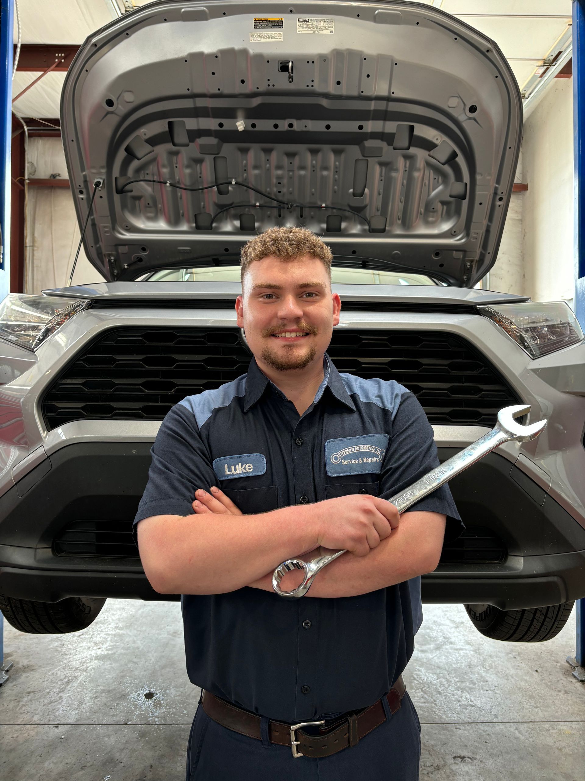 Mechanic with crossed arms holding wrench in front of a car | Stephen's Automotive