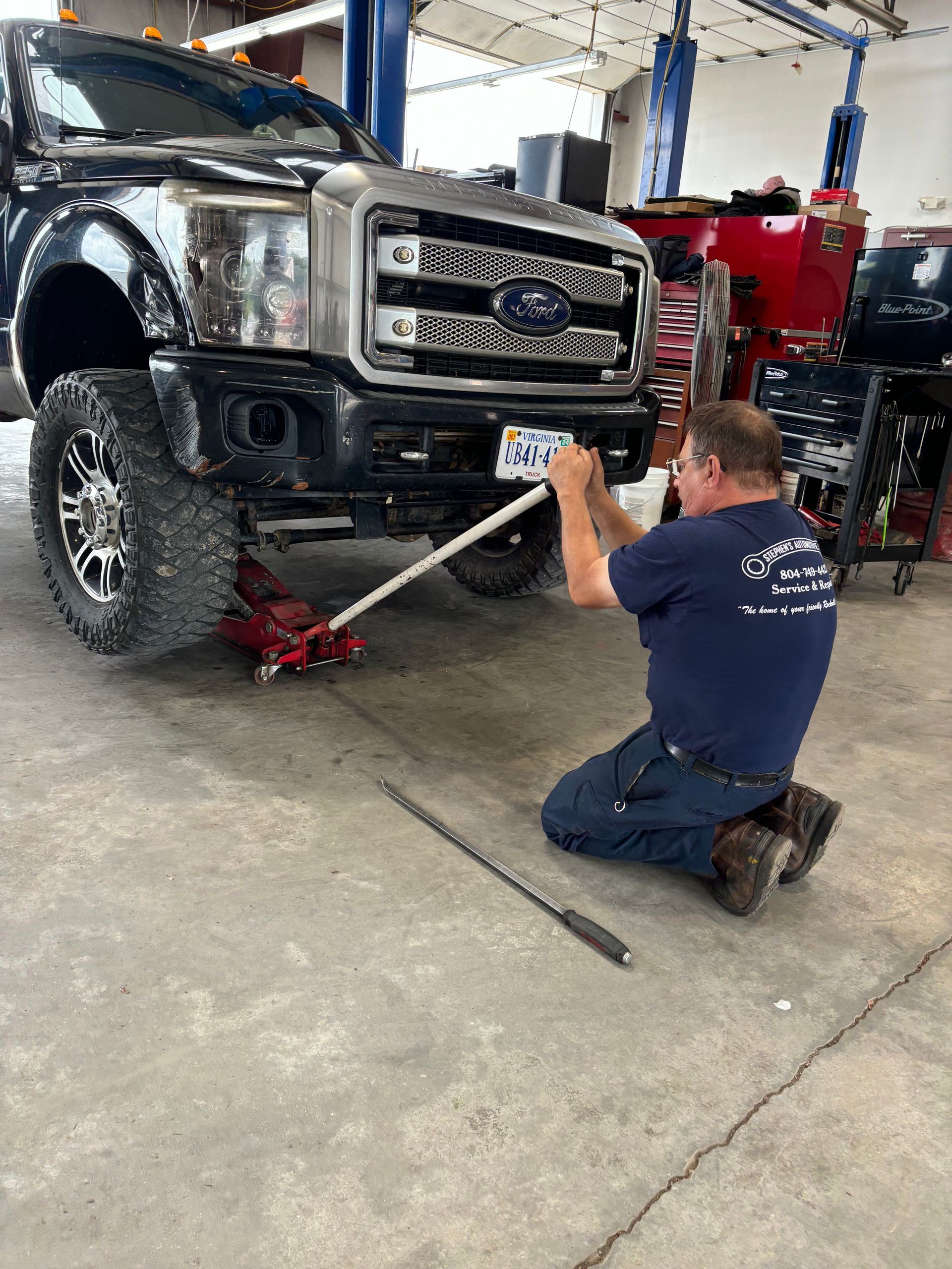 Mechanic kneeling, using a jack to lift a black truck | Stephen's Automotive