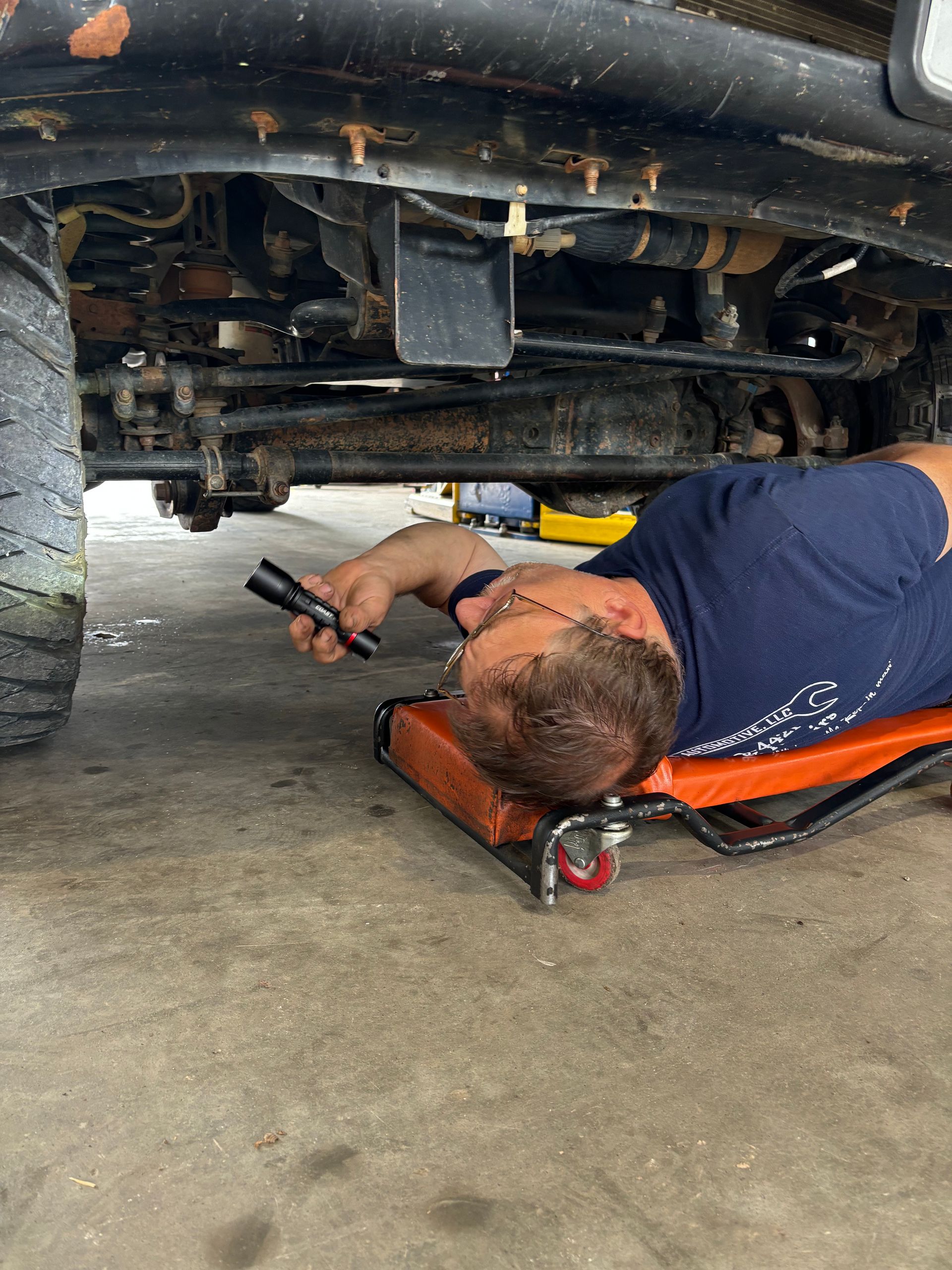 Mechanic on a creeper inspecting the underside of a vehicle with a flashlight | Stephen's Automotive