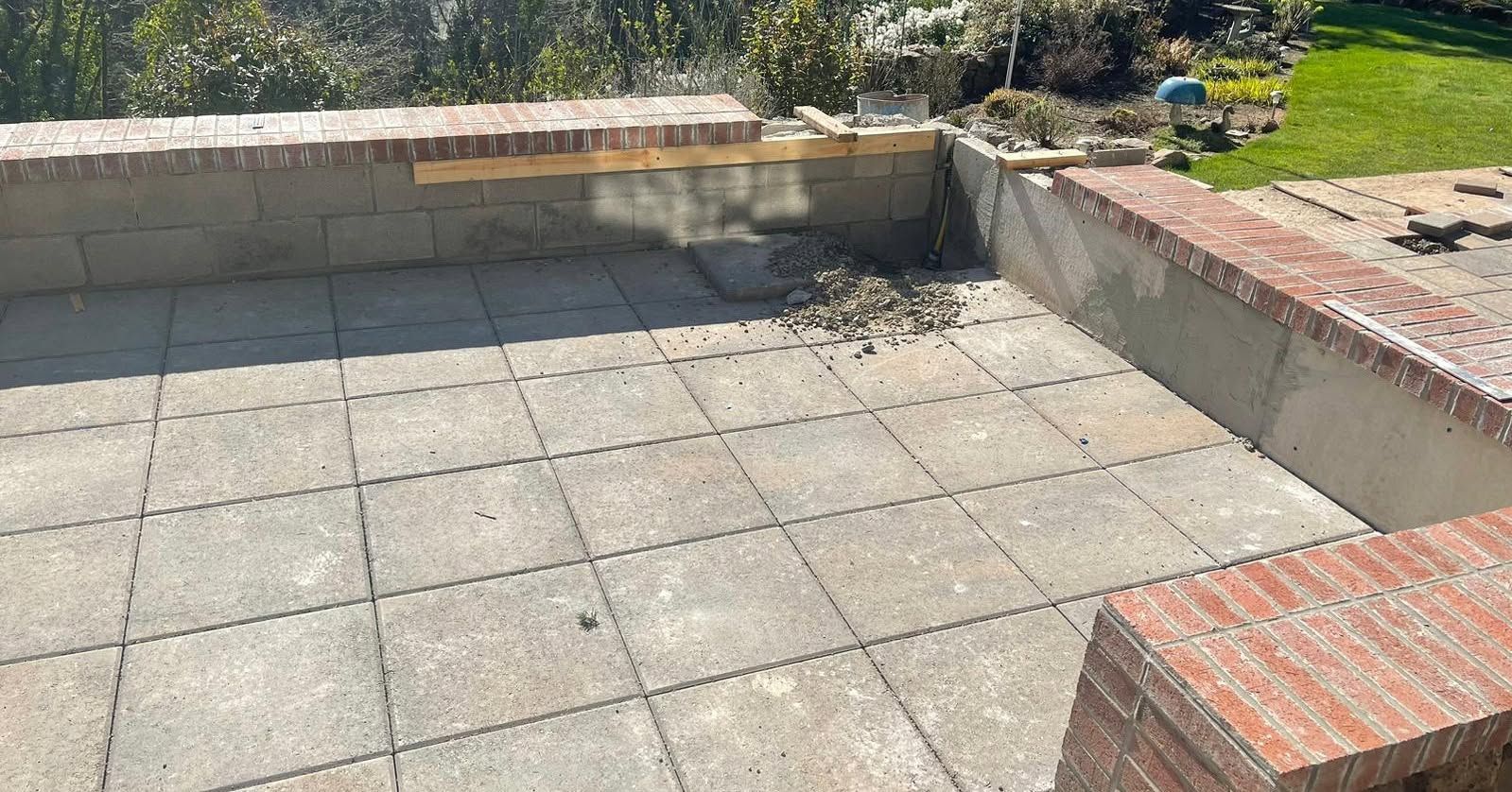 Patio with brick wall, concrete pavers, and construction debris. Sunny outdoor setting.