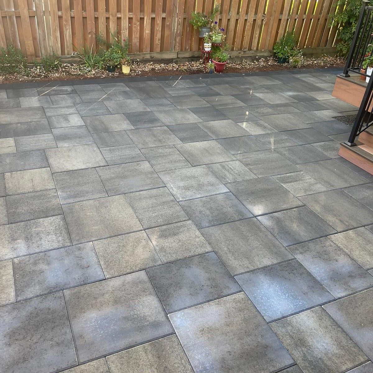 Gray patio pavers in a rectangular pattern, in front of a wooden fence.