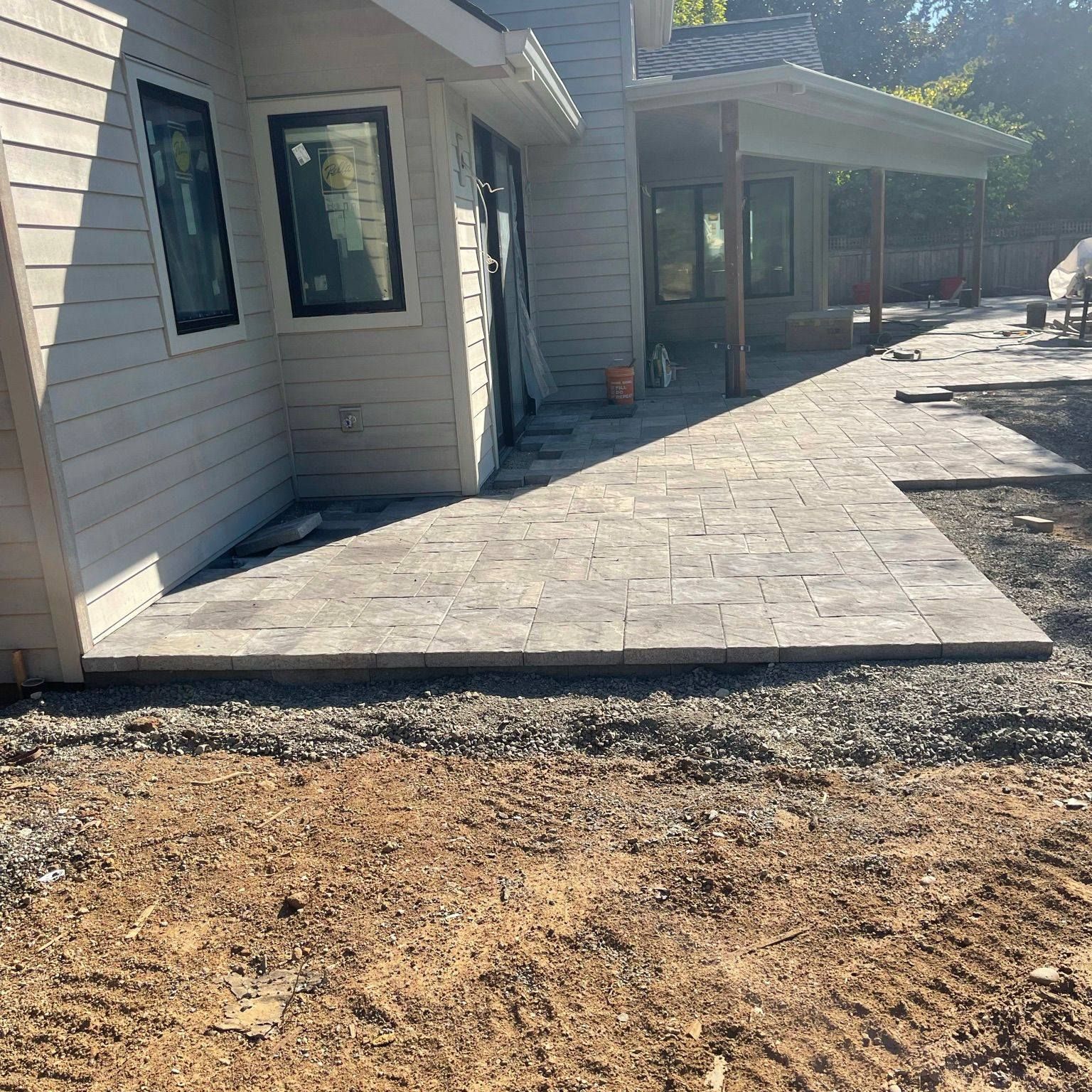 A patio under construction next to a house with light siding and dark-framed windows.
