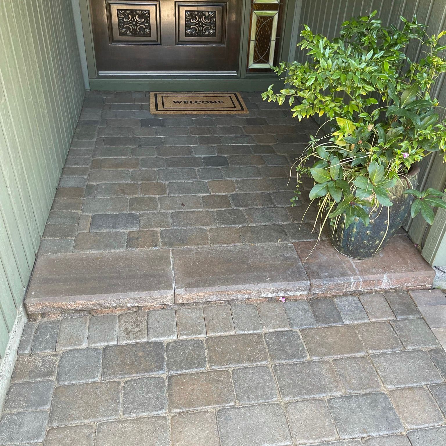 Brick pathway and steps leading to a dark wooden door. Potted green plant sits on the right.