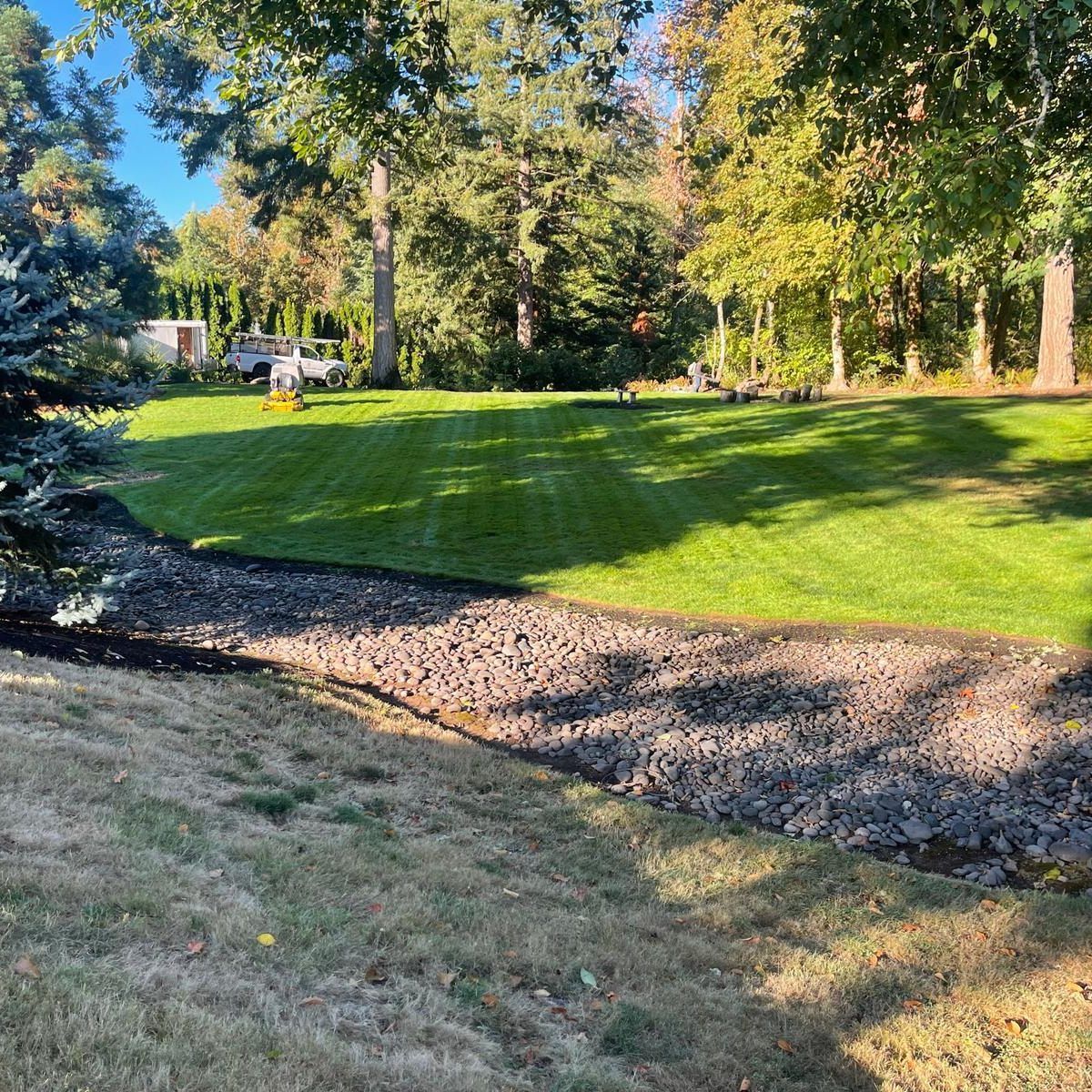 Lush green lawn with gravel border slopes downward. Trees in background, sunny day.