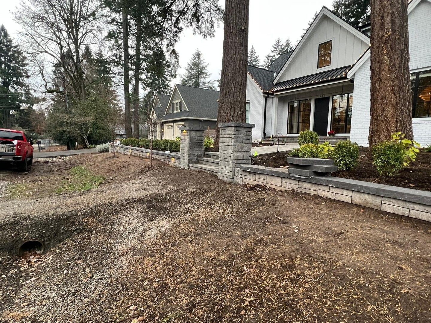 White house with stone pillars and retaining walls along a gravel driveway; trees in foreground.