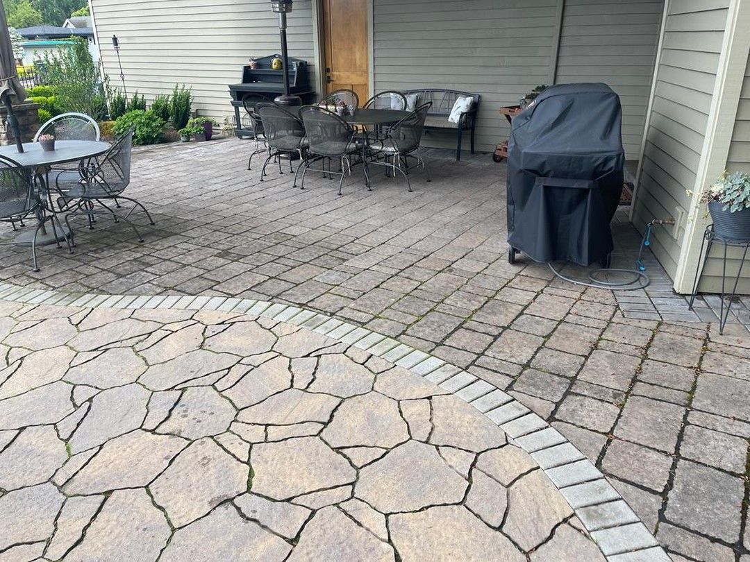 Stone patio with outdoor furniture, covered grill, and beige siding.