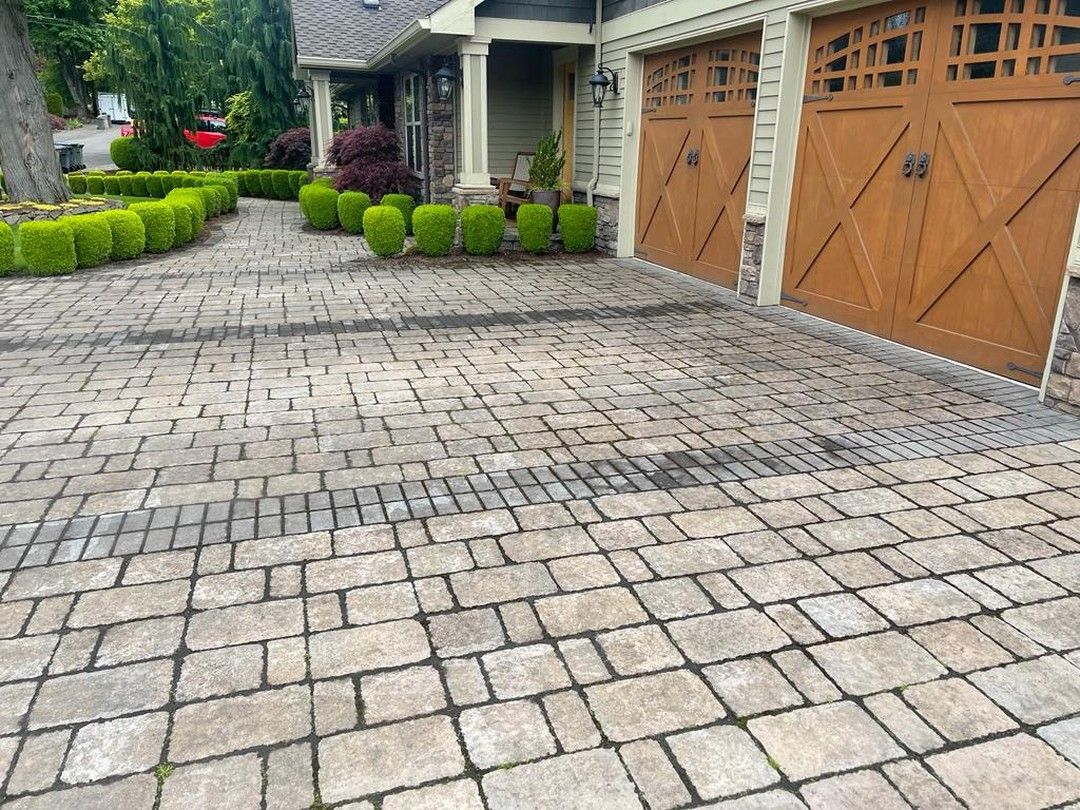 Brick driveway leading to a house with brown garage doors and manicured hedges.