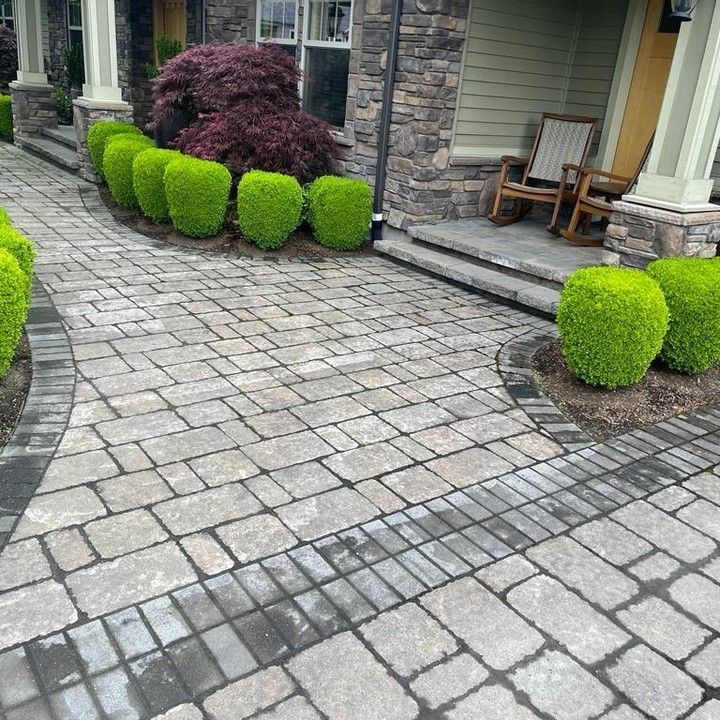 Brick pathway leading to a house with trimmed green bushes.