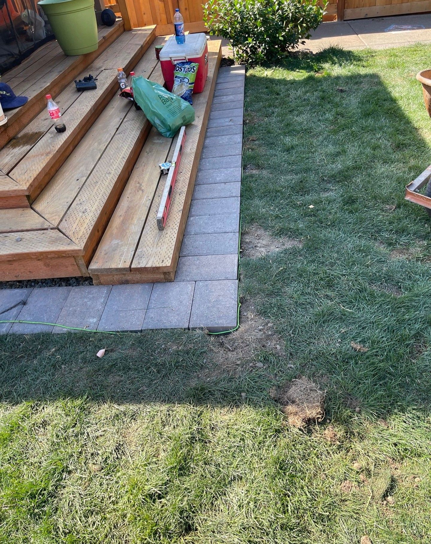 Wooden deck with paver border next to grass. Tools and cooler on deck.