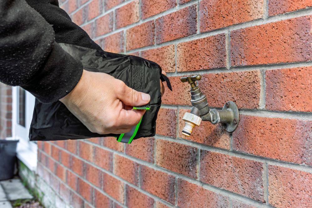 Person using a black faucet cover on an outdoor spigot attached to a brick wall.