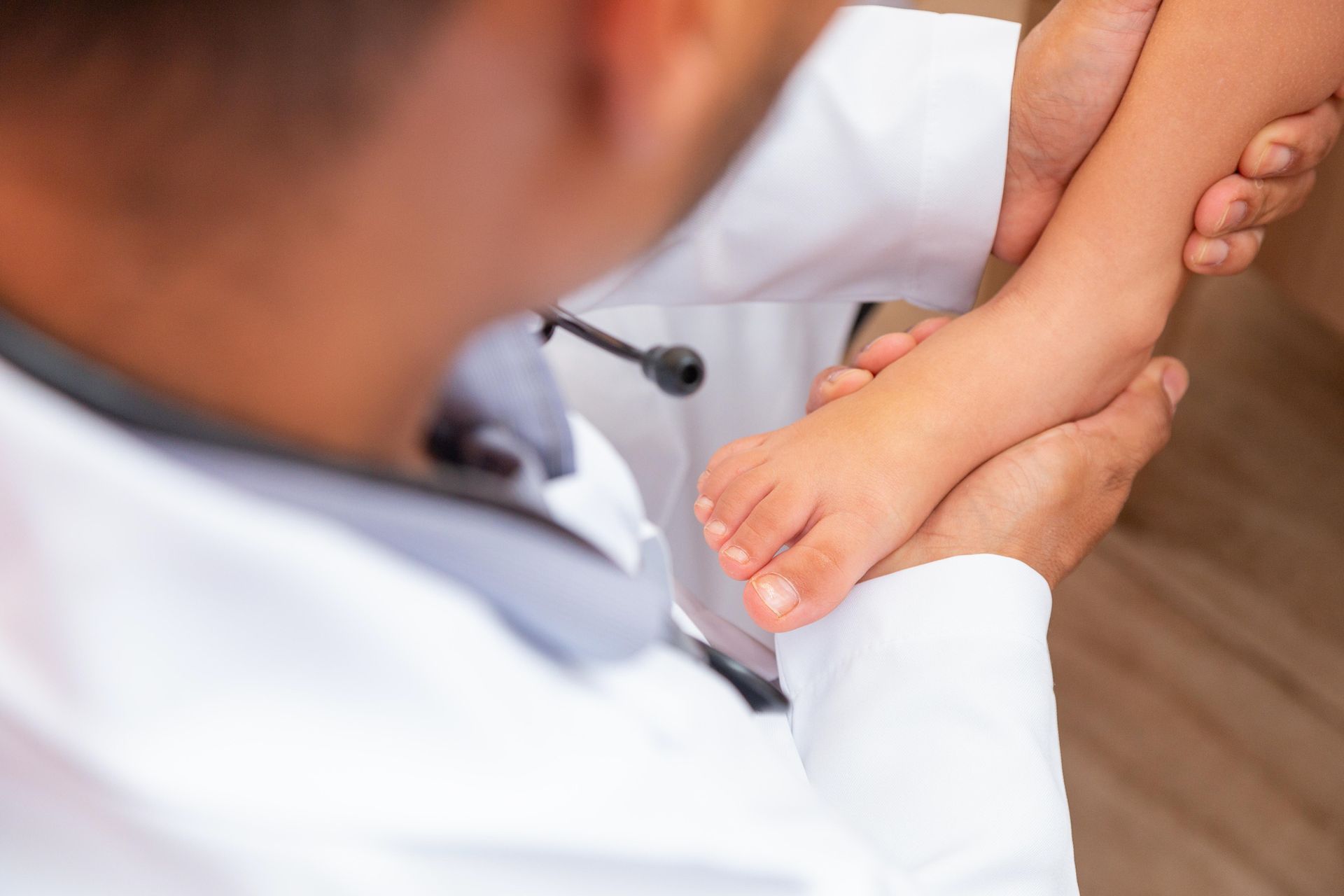 Doctor examining a child's back while she lies on an examination table. The doctor wears a white coat and stethoscope.
