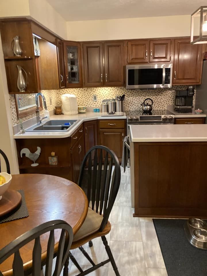 Kitchen with dark wooden cabinets, stainless steel appliances, and a round wooden table with chairs.