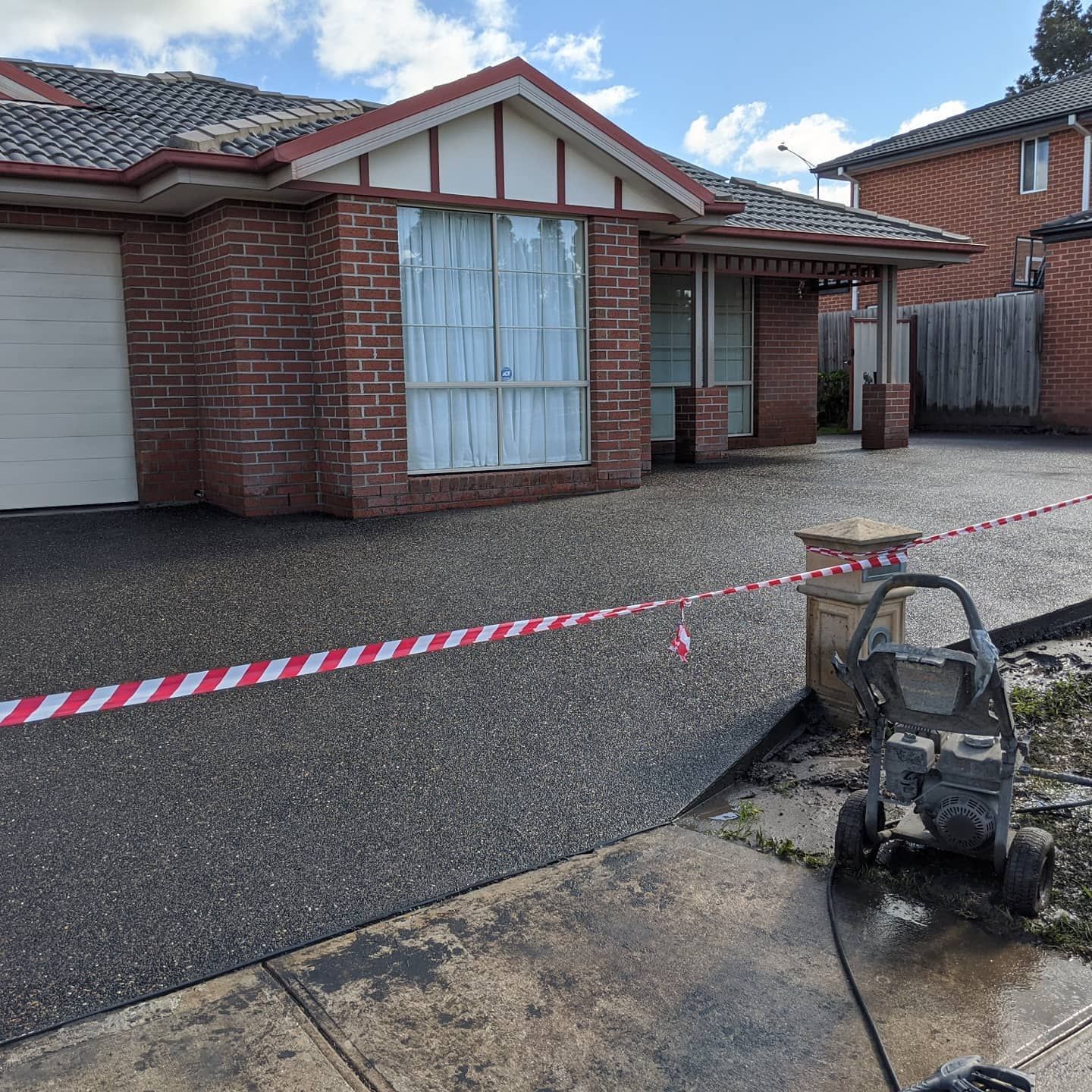 House with brick facade, driveway blocked by red and white tape. Pressure washer in foreground.