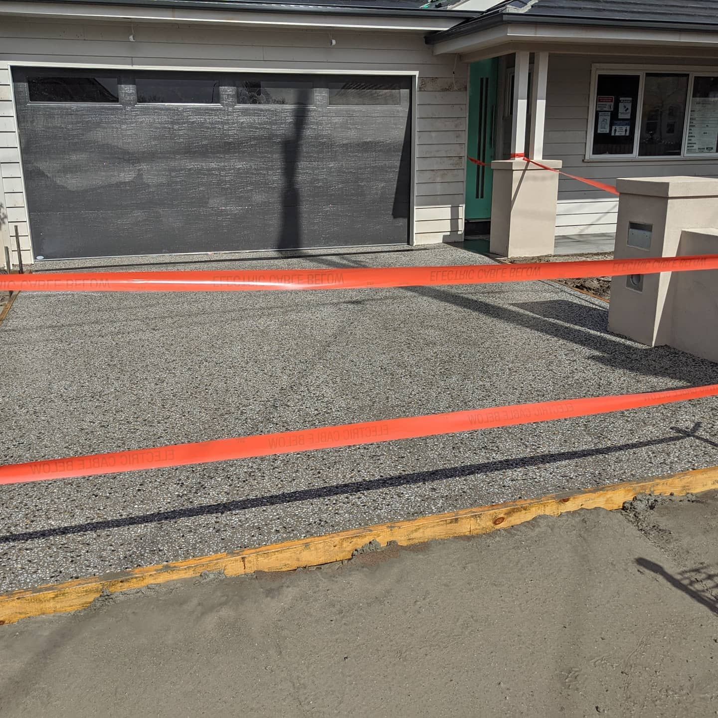Driveway resurfacing, with orange tape barrier in front of a garage, house in the background.