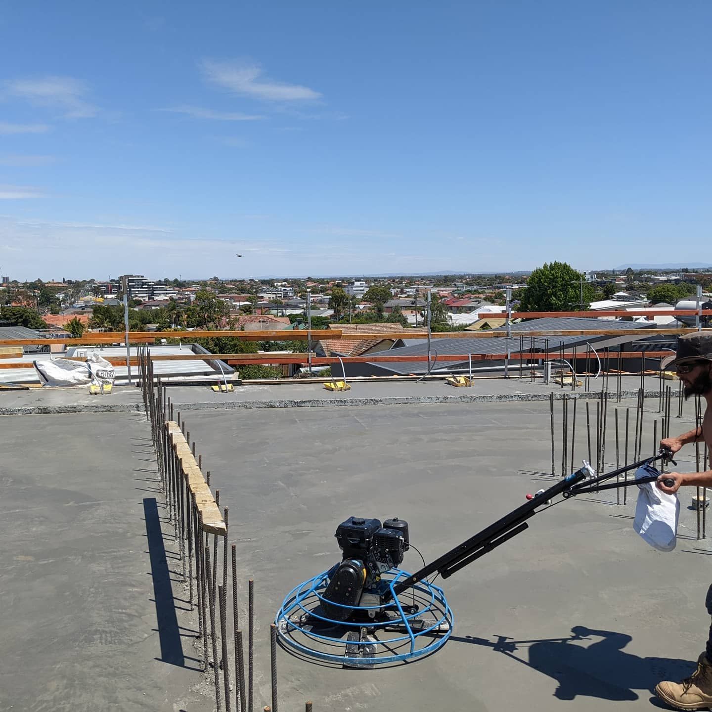 Man using a power trowel on a concrete rooftop, city in the background. 