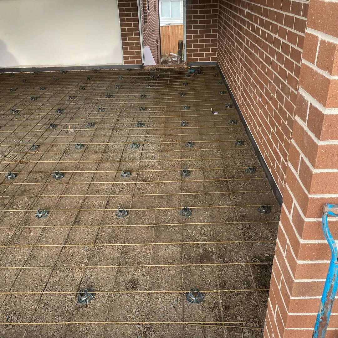 Construction site, exposed rebar grid on ground, near brick wall.