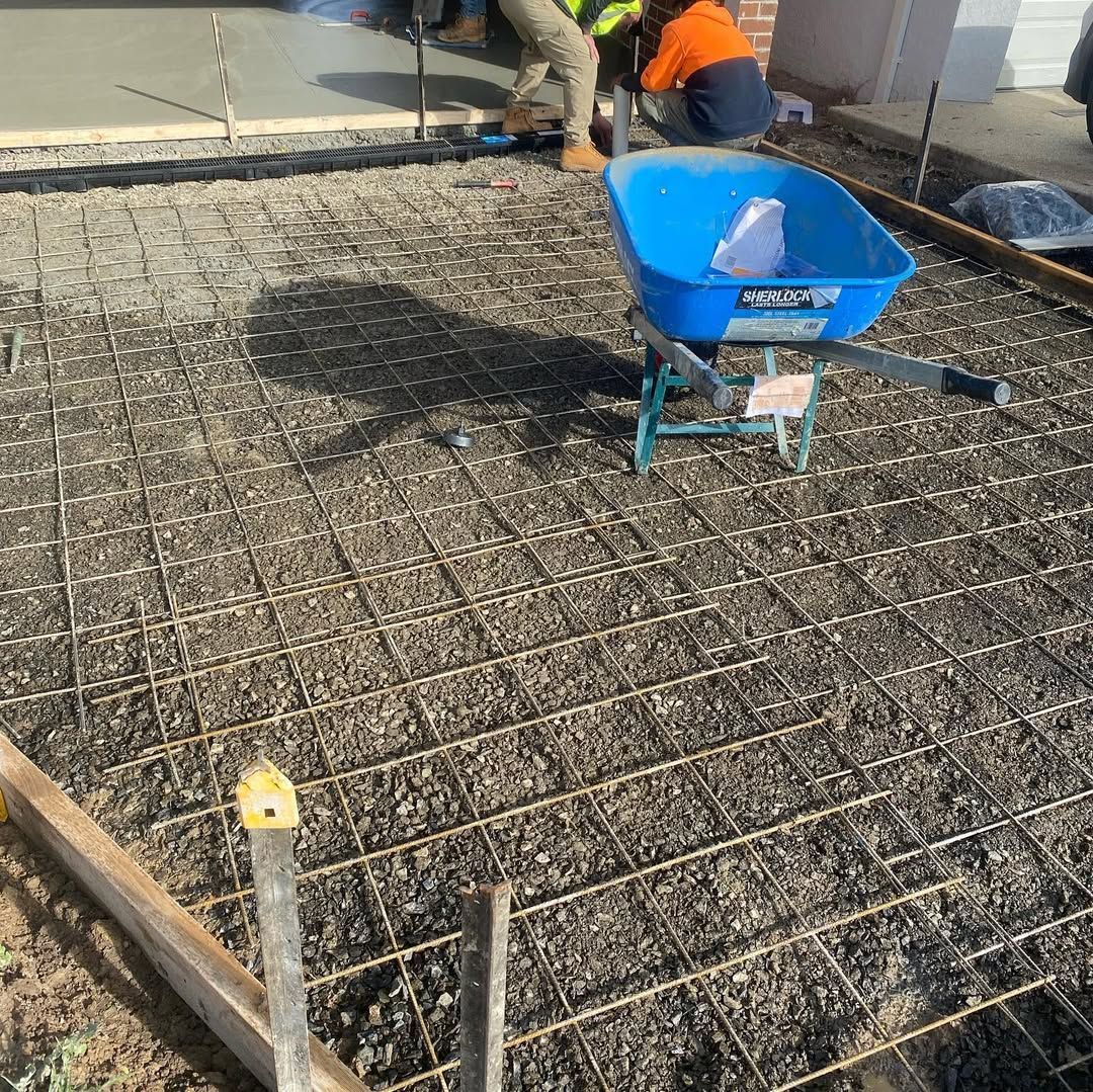 Concrete driveway with rebar grid, blue wheelbarrow, workers pouring concrete.