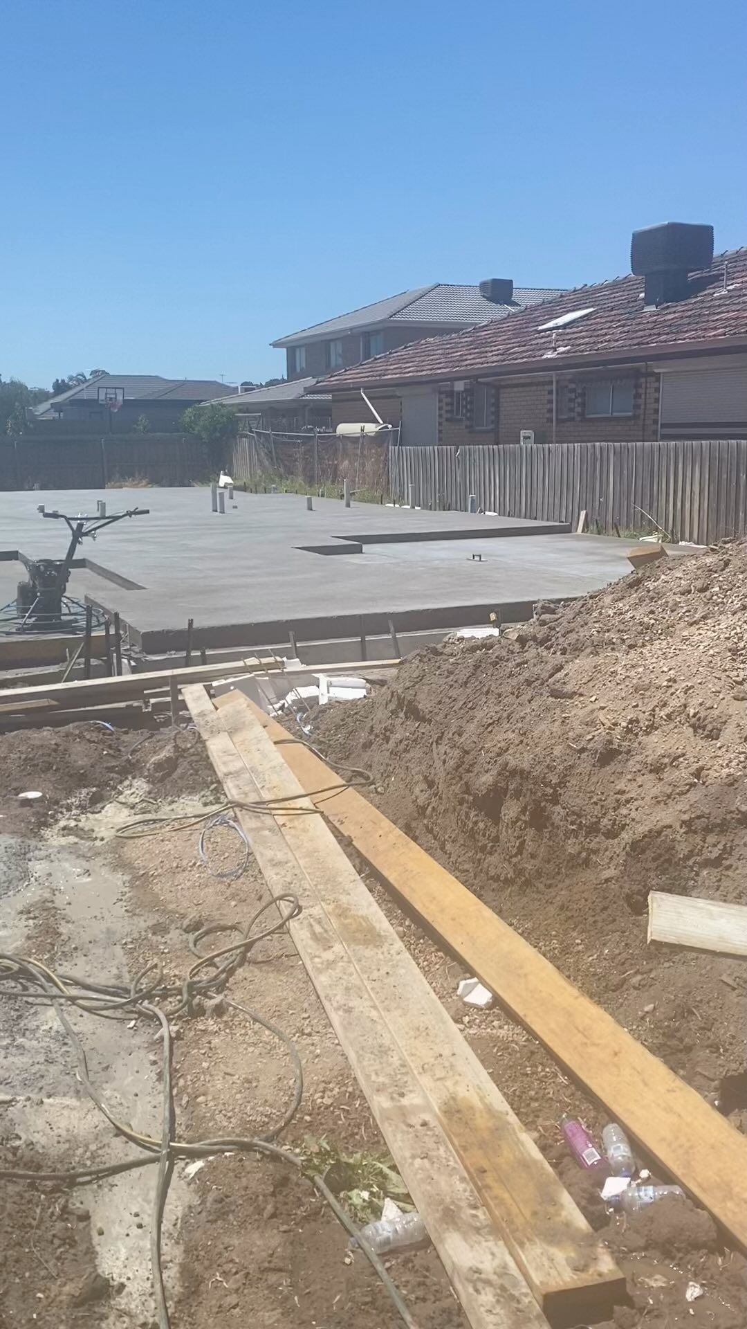 Construction site with poured concrete slab, wooden planks, and dirt.
