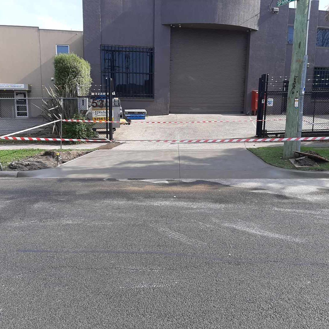 Exterior view of an industrial building with a closed gate, red and white tape, and a paved driveway.
