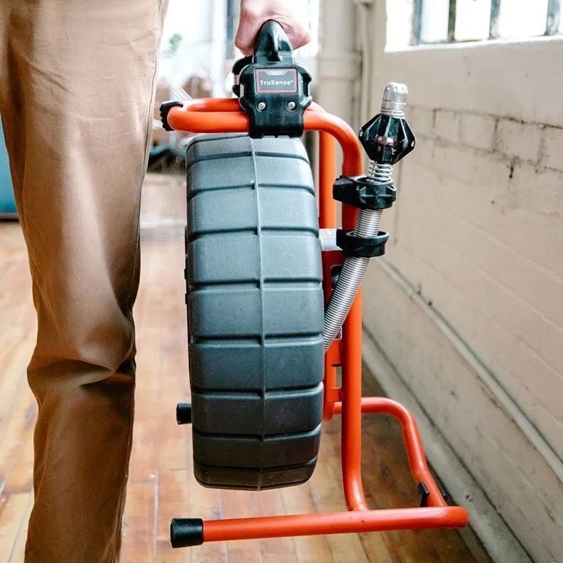 A person carrying a sewer inspection camera in a metal frame.