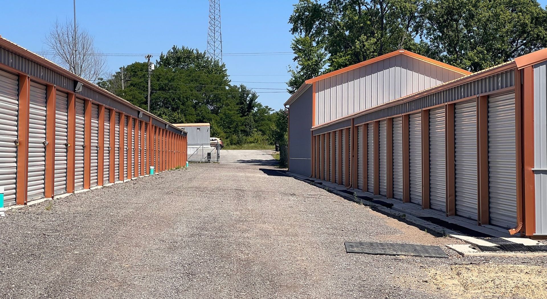 Storage units in a gravel driveway, with brown metal doors and gray walls under blue sky.