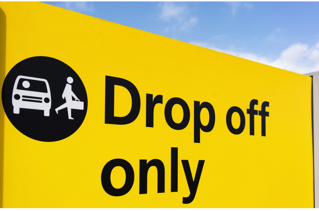 Airport yellow sign with black text and icons: Drop off only. Shows a bus and person with luggage.