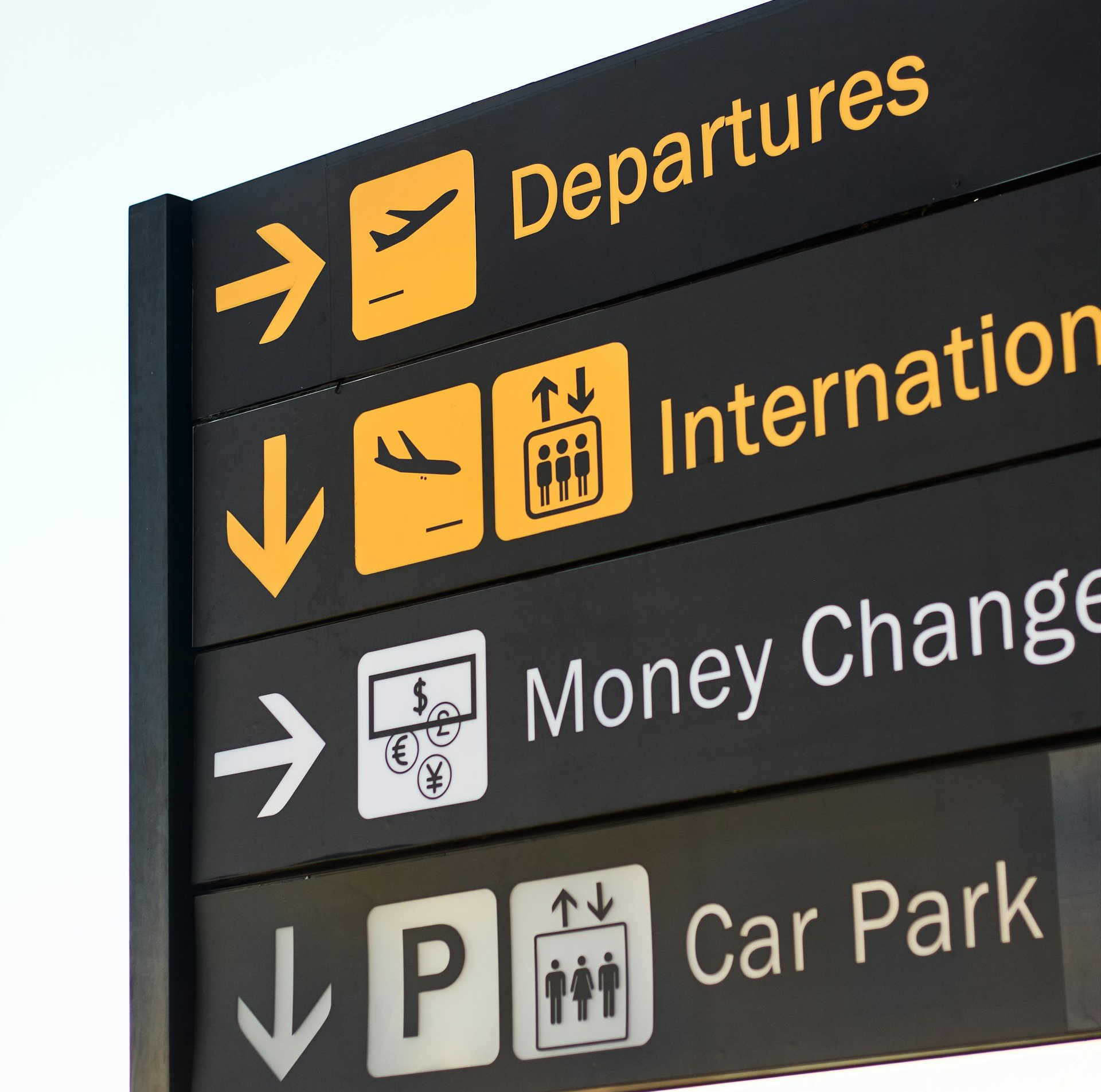 Airport sign with yellow text and icons on black background: Departures, International, Money Change, Car Park.