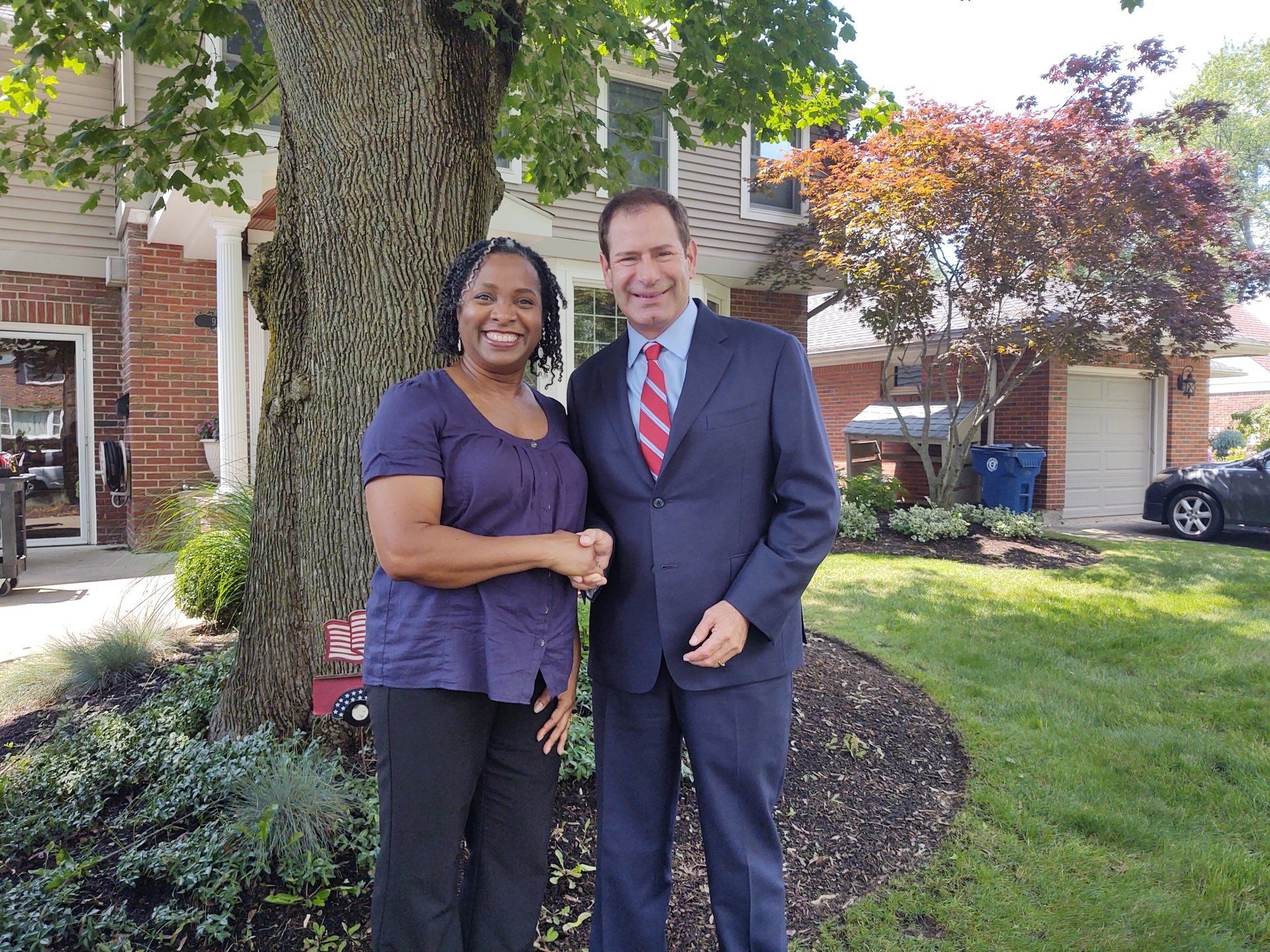 A man and a woman are shaking hands in front of a house