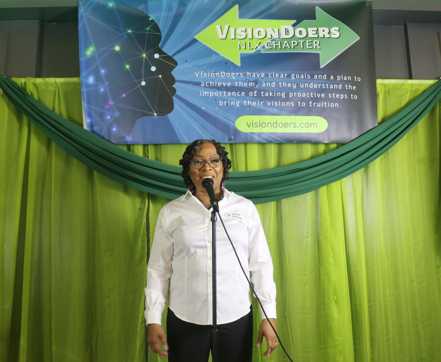 A woman singing into a microphone in front of a sign that says vision doers