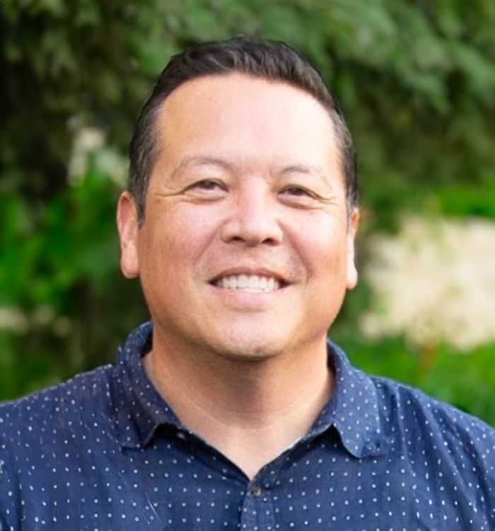 A man in a blue polka dot shirt is smiling for the camera.