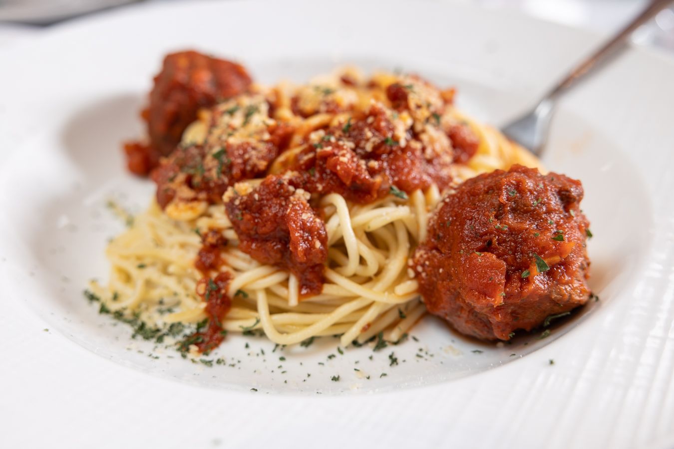 A white plate topped with spaghetti and meatballs with a fork.