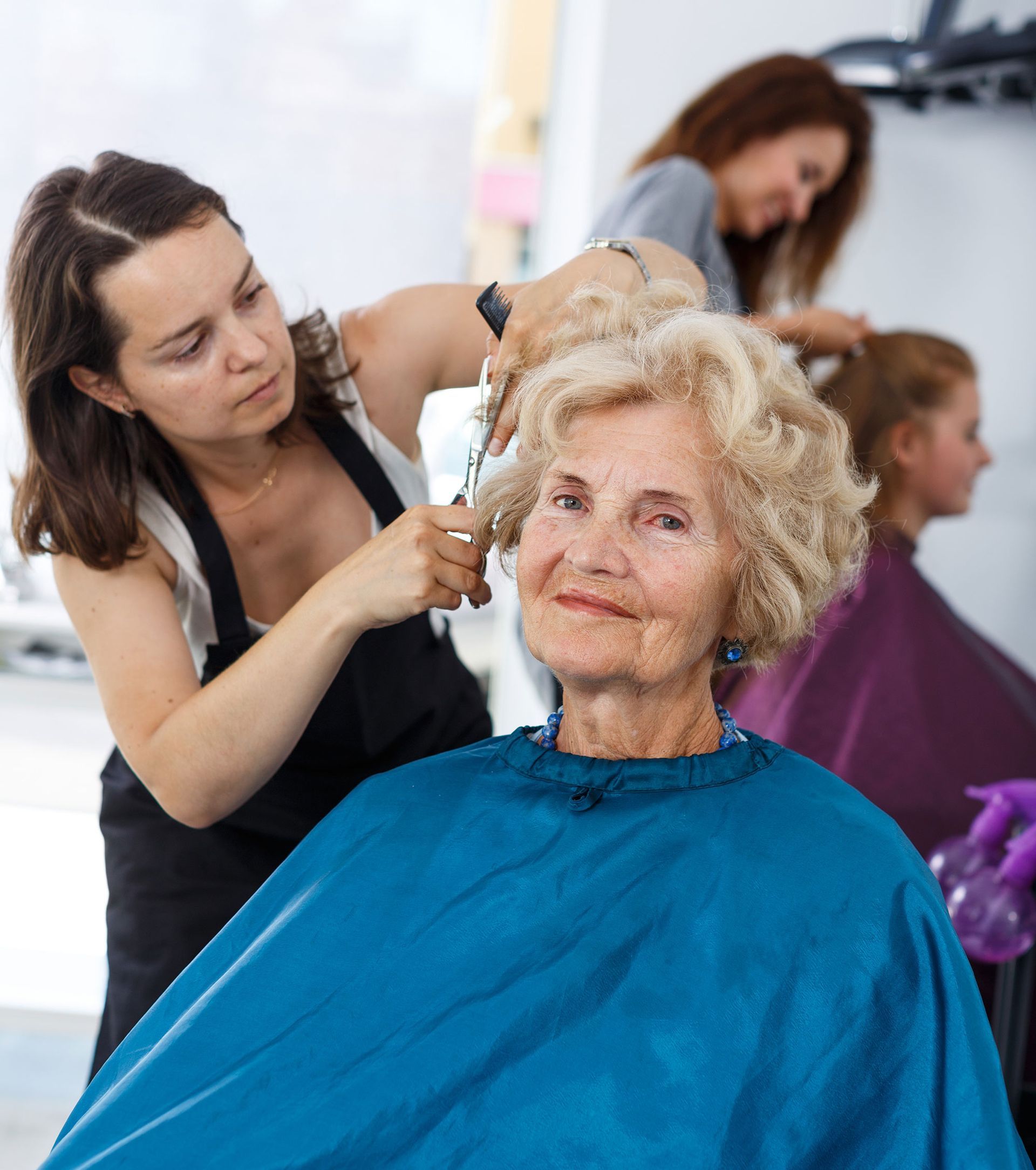 An older woman is getting her hair cut by a hairdresser